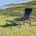 Folding camping recliner chair with footrest extended by the lake